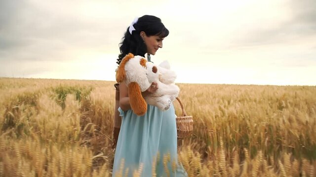 Pregnant caucasian lady walks in a meadow and is going to have a picnic on nature in slowmo. Woman expecting a baby carries pannier and toy. She is smiling and looking happy. Theme of resting outdoors