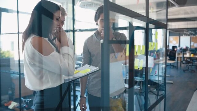 Young business people in formal clothes planning work in the office with paper stickers on the glass.