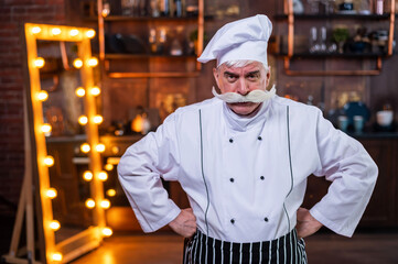 Fototapeta na wymiar Serious elderly male chef posing in the kitchen