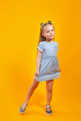 Adorable little model in trendy dress posing against bright yellow background
