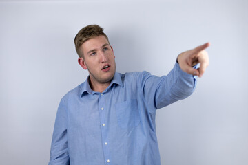 Fototapeta premium Business young man wearing a casual shirt over white background pointing with finger surprised ahead, open mouth amazed expression, something on the front