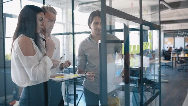 Young business people in formal clothes planning work in the office with paper stickers on the glass.