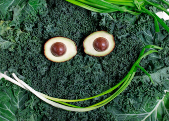 Cute face made of kale, avocado halves and green onion. Funny food. Healthy eating background