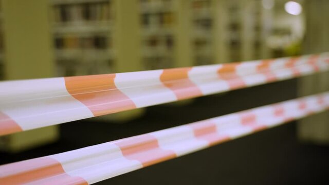 Public or school library closed with red and white no crossing police tape. Building with no people is shut down and blocked off with banner and do not cross striped line. Lockdown or crime scene zone