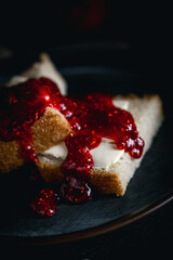 Sandwich with butter and raspberry jam on a dark plate with a dark background. Bread with butter and jelly in a black plate on a black background.