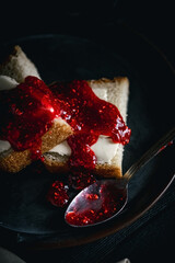 Sandwich with butter and raspberry jam on a dark plate with a dark background. Bread with butter and jelly in a black plate on a black background.