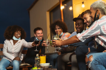 Happy multiracial friends having fun during holidays toasting with cocktails and red wine on patio...