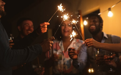 Happy young friends celebrating new year eve with sparklers fireworks and drinking cocktails on...