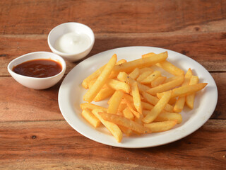 Golden fried French fries with tomato ketchup and mayonnaise served in a plate over a rustic wooden background, selective focus