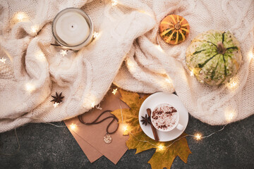 Top view, flat lay. Autumn-winter composition in brown-beige colors in the hygge style. Cozy knitted blanket, garland, small pumpkins, a cup of hot cappuccino.