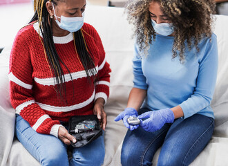 Young nurse woman and senior african patient waiting for the diabetes test result while wearing surgical face mask for coronavirus outbreak