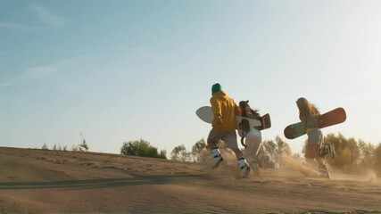 Three cheerful multiratial friends enjoying summer vacation. Young hipster guys with sandboard in hands running high at shining sunset. Holidays, sport, journey, travel, happiness, friendship concept.
