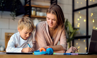 mom helping young son with laptop to do homework. Young woman teaching little boy to use the computer. baby sitter teaching little child girl use laptop application.