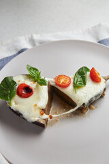 Baked eggplant with mozzarella cheese, cherry tomatoes and basil on a grey plate and blue tablecloth. Recipe of Italian cuisine. Christmas and New Year snacks and ready meals.