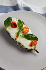 Baked eggplant with mozzarella cheese, cherry tomatoes and basil on a grey plate and blue tablecloth. Recipe of Italian cuisine. Christmas and New Year snacks and ready meals.