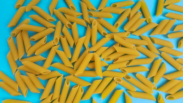 Animated raw pasta on a blue background, top view. Stop motion animation of a large amount of pasta.