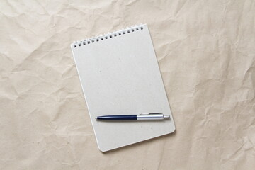  Gray notepad with white coiled spring and pen on a background of beige crumpled craft paper