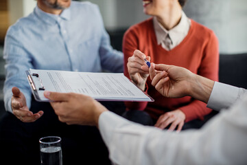 Close-up of unrecognizable couple signing a contract with financial advisor.