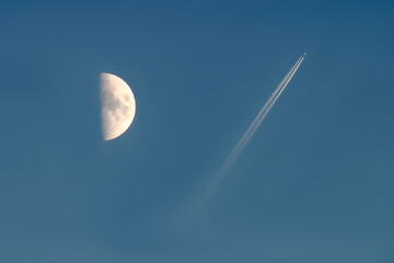 illuminated half moon and trail from an airplane in the blue sky