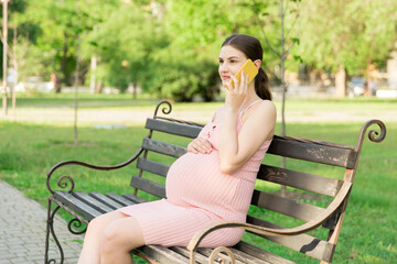 pregnant woman sits on a park bench and talking on phone