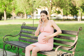 pregnant woman sits on a park bench and talking on phone