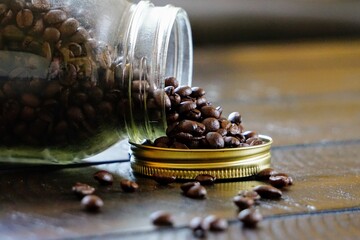 Jar with coffee beans on its side spilling out on wood table 