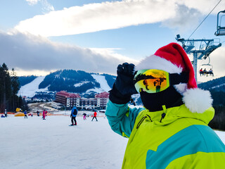 happy man in ski outfit with santa red christmas hat at winter mountains hill
