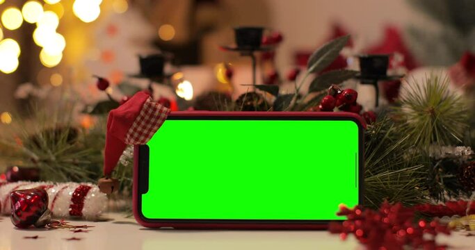 iPhone Xs Max smartphone with pre keyed green screen and Santa Claus' hat on top standing in front of Christmas background. Easy to paste your content. Dolly Shot