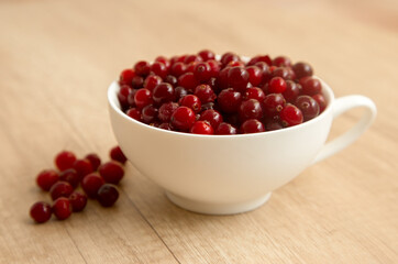 red cranberries in a white cup on a wooden background