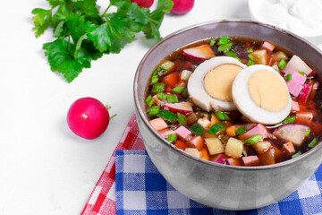 Russian cold soup Okroshka with vegetables, sausage, eggs and kvass in a bowl on the white table
