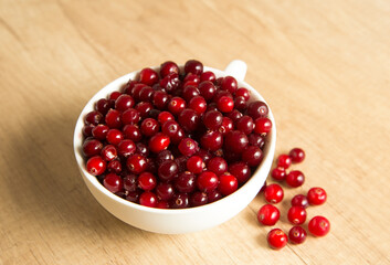 red cranberries in a white cup on a wooden background