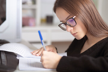 Preparation for exams. Young teenage girl at home studies, writes, reads, remembers