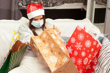 Merry Christmas and happy new year, Young woman in quarantine wearing a medical mask at home looks at gifts in bags with winter patterns during the coronavirus epidemic
