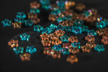 Star-shaped multicolored beads are scattered on a black background. Needlework materials close-up.