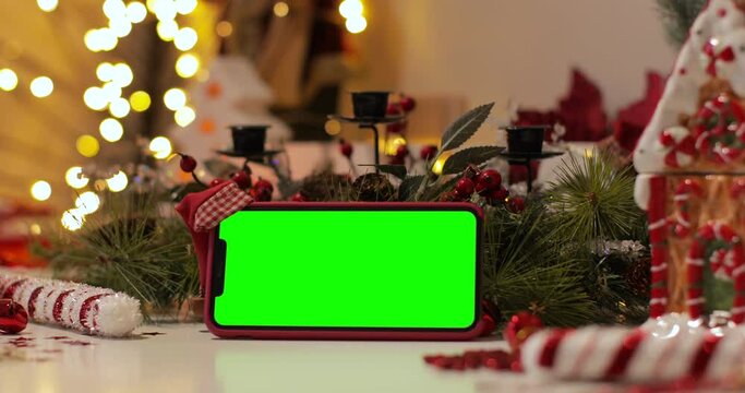iPhone Xs Max smartphone with pre keyed green screen and Santa Claus' hat on top standing in front of Christmas background. Easy to paste your content. Zoom in shot