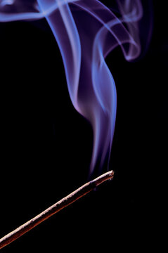 vertical photo of a smoking incense stick in violet color