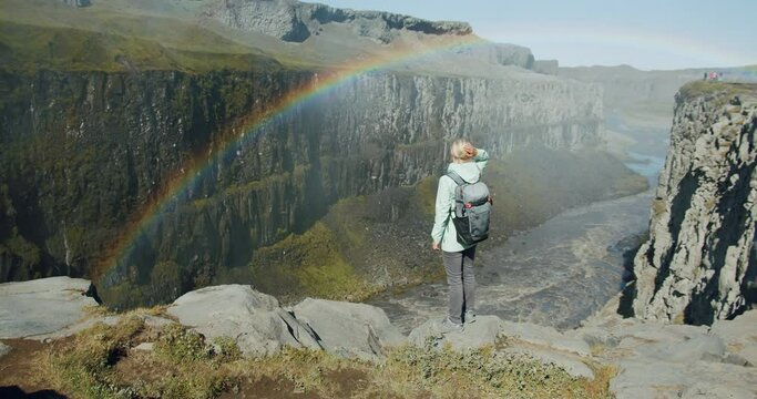 Woman standing at cliff edge looking down the canyon with river near Detifoss waterfall in Iceland