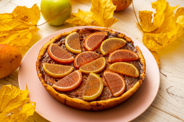 Pumpkin pie on a white wooden background. Yellow autumn leaves, apples and pears.