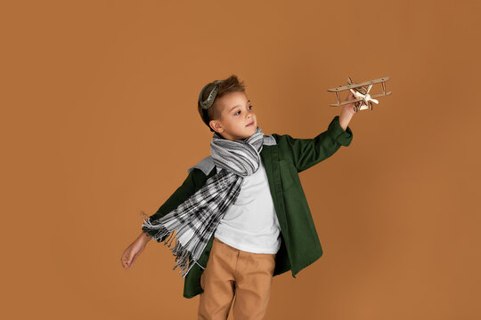 happy child boy playing with wooden toy airplane on studio background. kid dreams of traveling