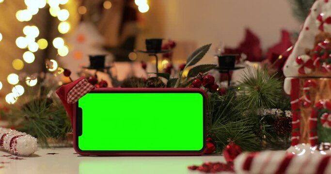 iPhone Xs Max smartphone with pre keyed green screen and Santa Claus' hat on top standing in front of Christmas background. Easy to paste your content. Slider shot