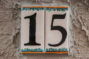 Weathered grunge square faience enameled decorated plate of number of street address with number 15 closeup