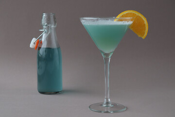 Composition of blue lagoon cocktail decorated with a slice of orange with a bottle on grey background