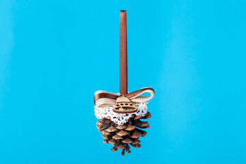 pine cone toy decoration for a Christmas tree with a brown ribbon bow, decor object hanging gift for the New Year holidays isolated on a blue background with copy space, nobody.