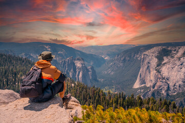 A young man on the trek sitting on the Sentinel Dome lookout in Yosemite National Park looking at...