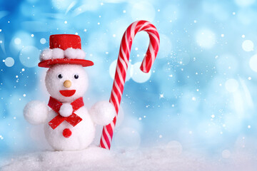 Cute decorative snowman with candy cane on blue background, bokeh effect. Space for text