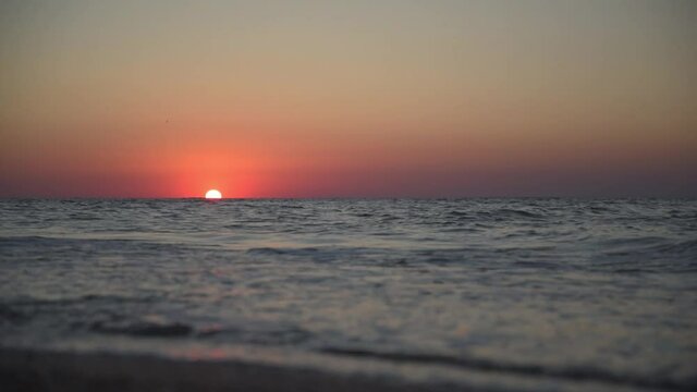Calm picture of a sea sunset. The red sun sets in the sea. Incoming waves. The sky is colored red