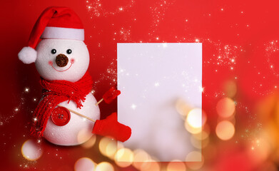 Decorative snowman with blank white card on red background, bokeh effect. Space for text