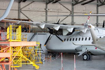 White passenger turboprop airplane under maintenance in the hangar. Repair of aircraft engine on the wing and checking mechanical systems for flight operations