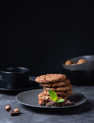 a stack of chocolate chip cookies with chocolate chips, nuts and mint  on a dark table