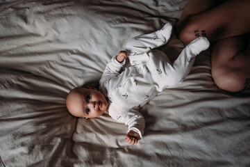 the child lies on the bed in a bodysuit next to mom